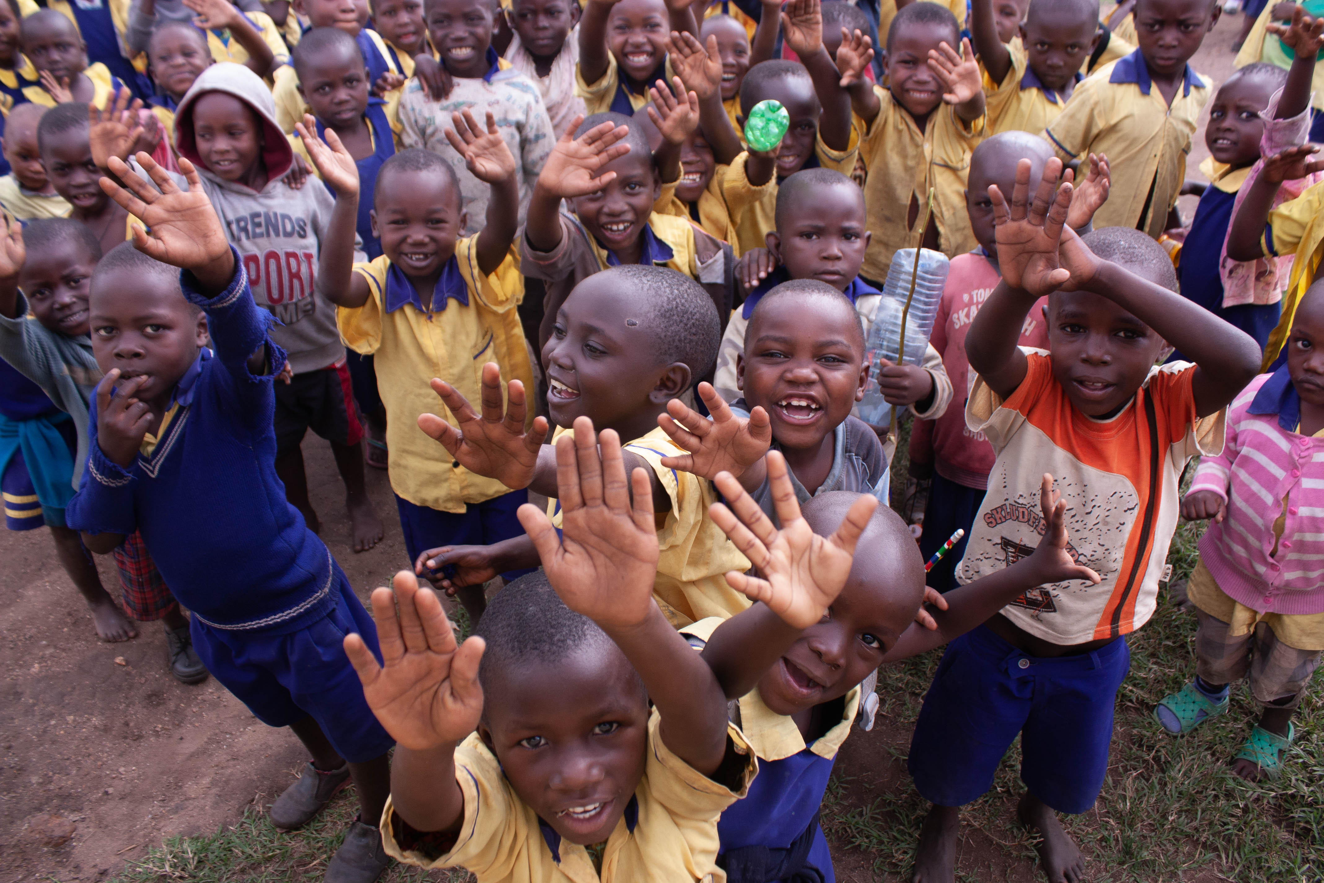 A group of school children excitedly smile and wave at the camera.